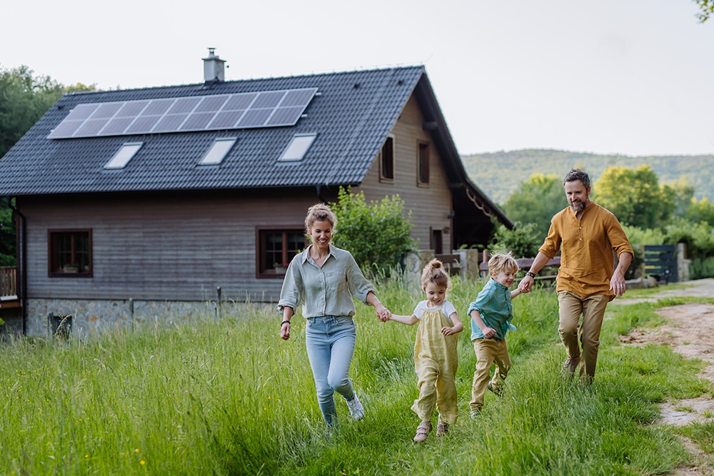 Happy family in front of their house with solar panels on the roof.